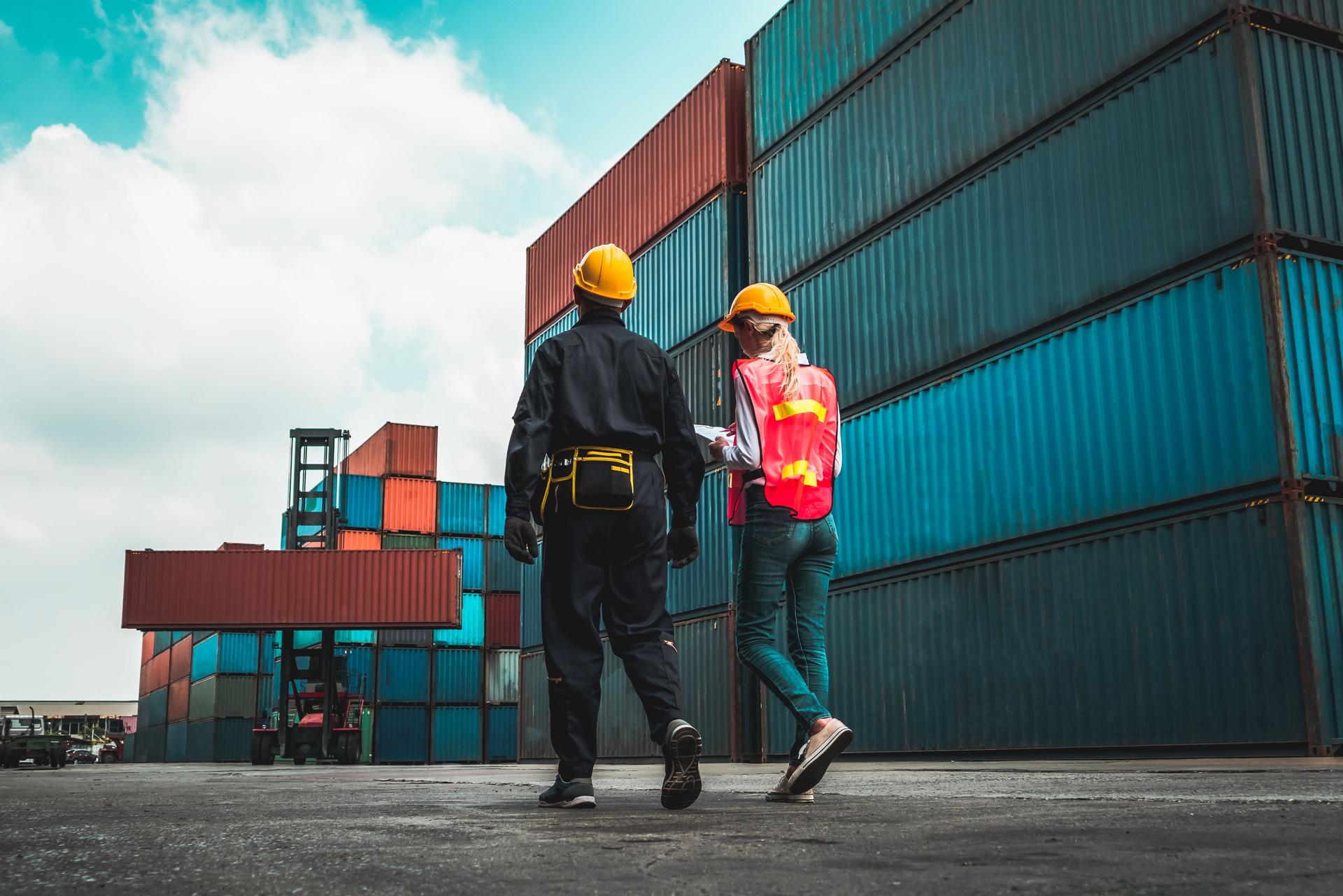 Industrial worker works with co-worker at overseas shipping container yard . Logistics supply chain management and international goods export concept .